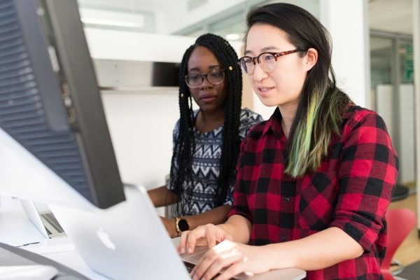 Two women working on a computer project together in an office setting.